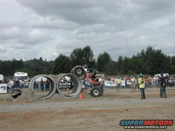 Off-road buggy driving through concrete pipes at an event with spectators.