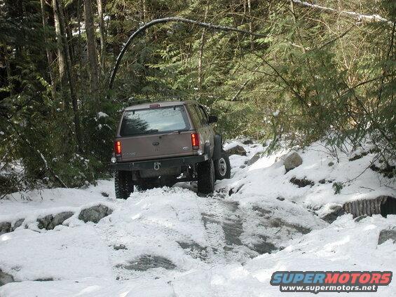 Tan Ford Explorer driving on a snowy trail in a forest.
