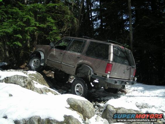 Brown Ford Explorer off-roading on a snowy, rocky trail.