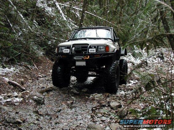 Lifted off-road pickup truck on a snowy, rocky trail in a forest.