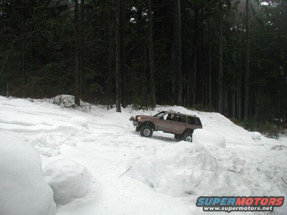 Brown Ford SUV driving through snow in a forest.