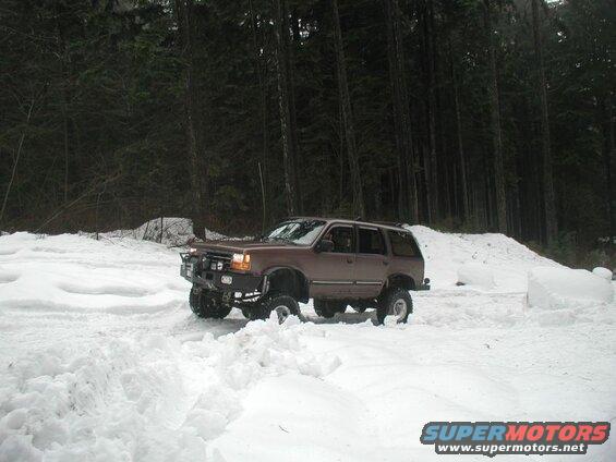 Lifted brown SUV driving through deep snow in a forest.