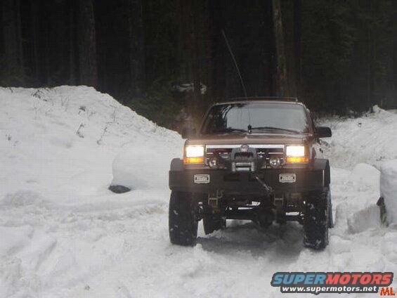 Lifted brown SUV with winch in deep snow, headlights on.