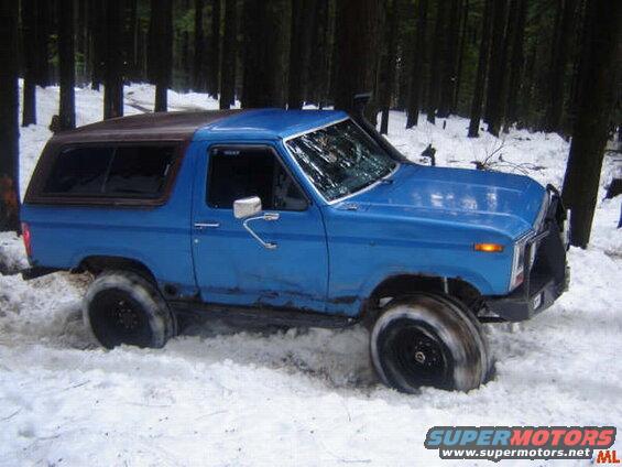 Blue Ford Bronco stuck in snow in a forest, cracked windshield.