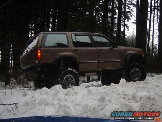 Lifted brown SUV driving through snow in a forest.