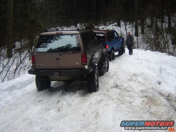 Tan and blue SUVs on a snowy forest road with a person standing by the blue SUV.