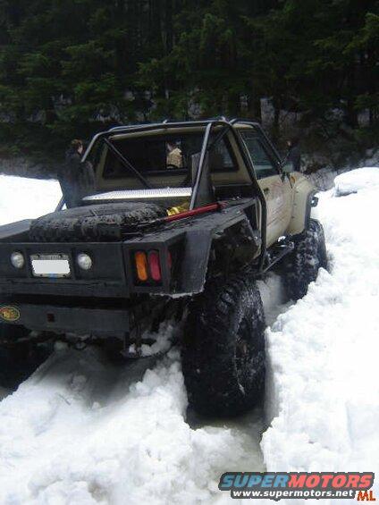 Modified pickup truck with large tires driving through deep snow.