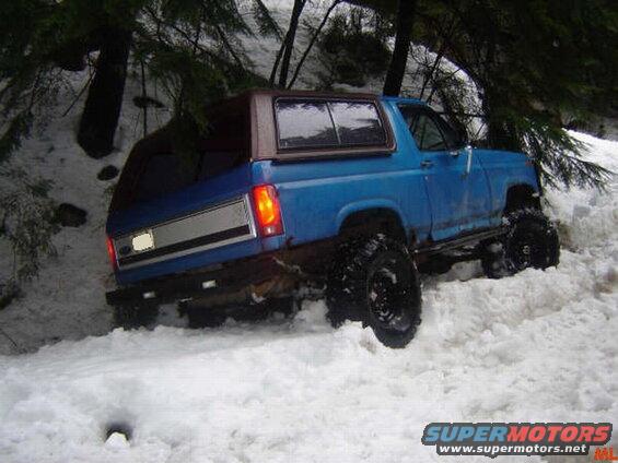 Blue Ford Bronco with large tires stuck in snow, rear view.