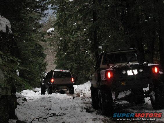 Two off-road vehicles on a snowy forest road. One is a modified pickup, the other an SUV.