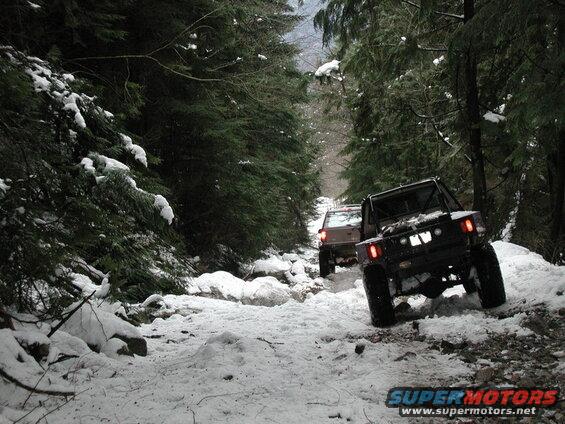 Two off-road SUVs driving on a snowy forest trail.