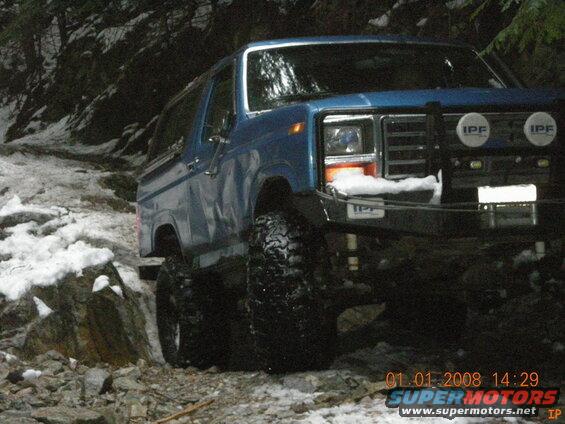 Blue Ford Bronco with off-road tires and IPF lights on a snowy trail.