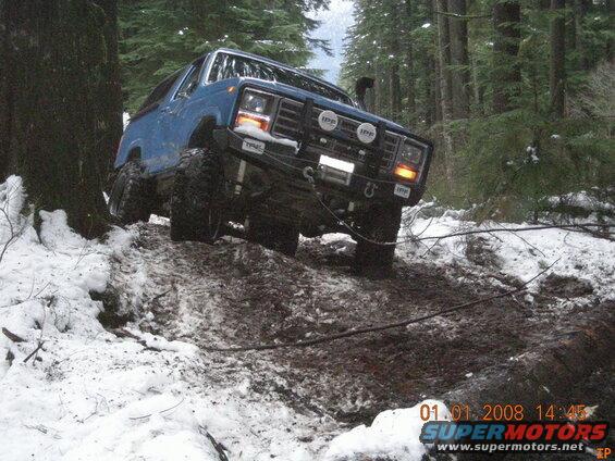 Blue Ford Bronco on a muddy, snowy forest trail.