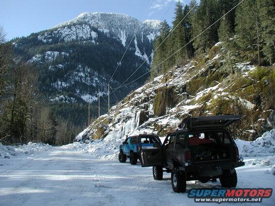 Two SUVs parked on a snowy mountain road, one with its rear hatch open.