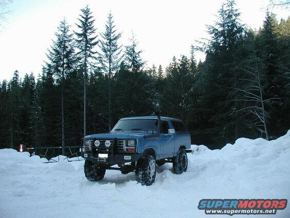 Blue Ford Bronco in snow with forest background and gate
