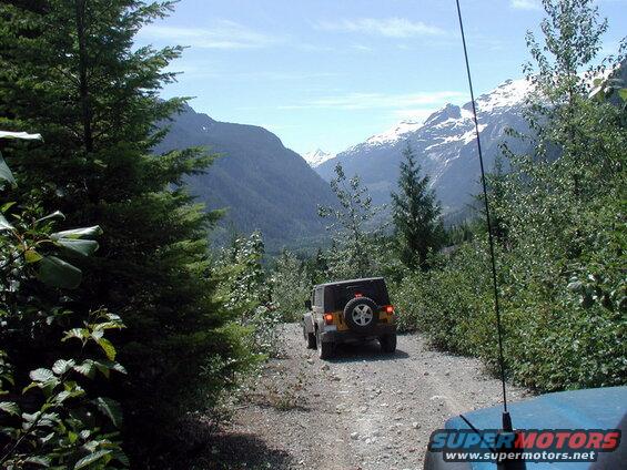 Yellow Jeep Wrangler driving on a gravel road in a mountainous forest.