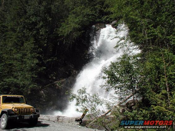 Yellow Jeep Wrangler parked by a waterfall in a forest.