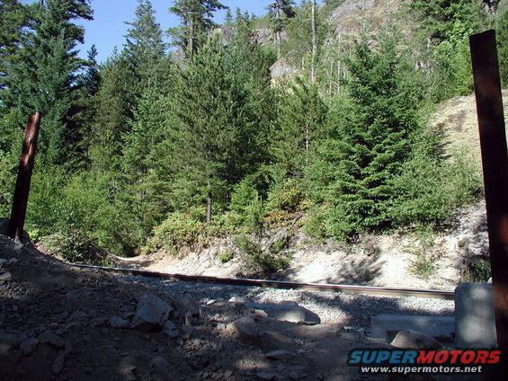 Railroad tracks in a forest with a rocky hillside.