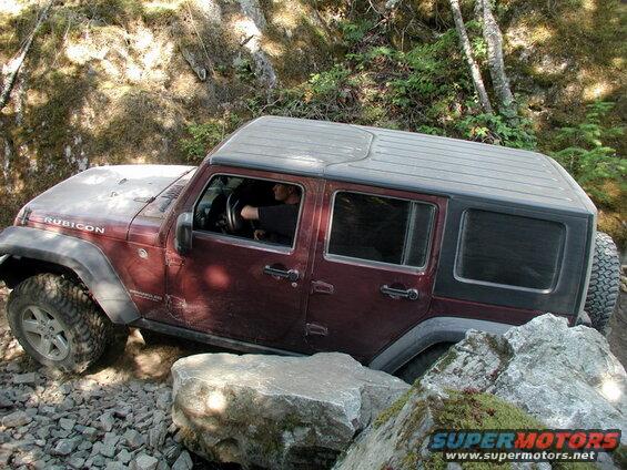 Maroon Jeep Wrangler Rubicon off-roading over rocks and boulders.
