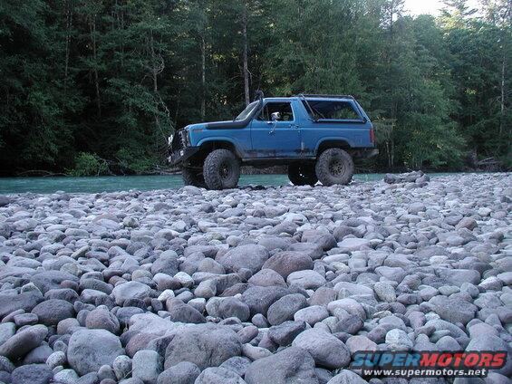 Blue Ford Bronco parked on a rocky riverbed next to a turquoise river.