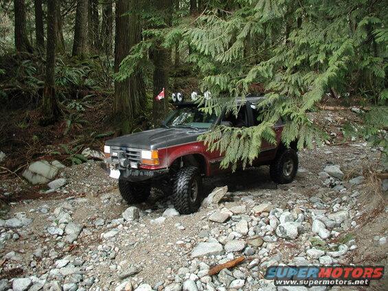 Lifted red and gray Ford Explorer on a rocky forest trail.