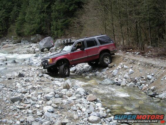 Red and gray SUV off-roading through a rocky riverbed.