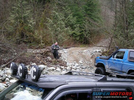Blue Ford Bronco with snorkel on a rocky trail, man standing nearby.