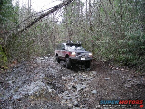 Off-road Ford Explorer on a muddy, rocky forest trail.