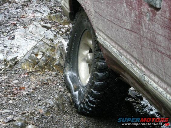 Right rear tire and fender of a maroon SUV on a rocky trail.