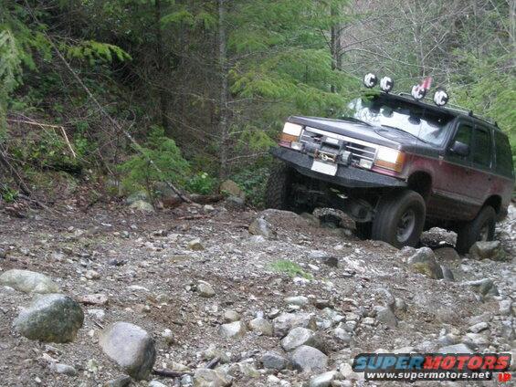 Maroon Ford Explorer off-roading on a rocky trail with a custom bumper and lights.