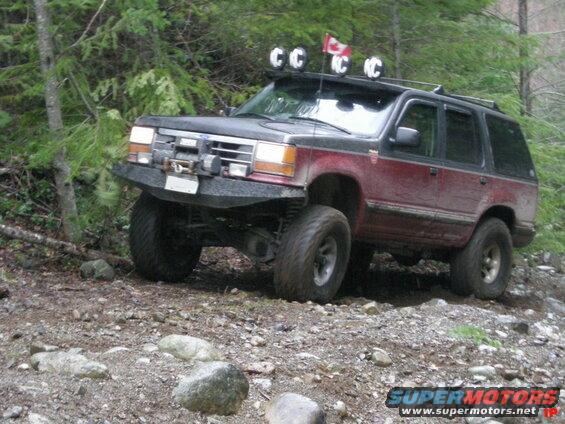 Red and black Ford Explorer off-roading on a rocky trail with KC lights.