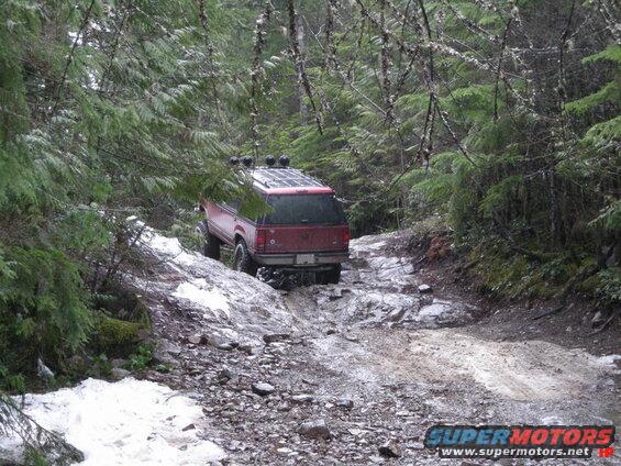 Red SUV on a challenging off-road trail in a forest.