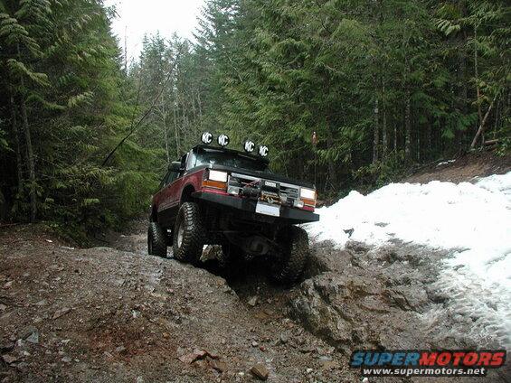 Lifted red Ford Explorer off-roading on a muddy, rocky trail with snow