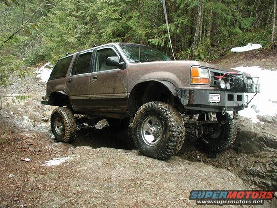 Lifted brown Ford Explorer off-roading on a muddy trail with snow.