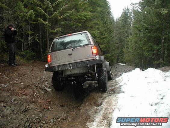 Tan Ford SUV on a muddy and snowy forest trail.
