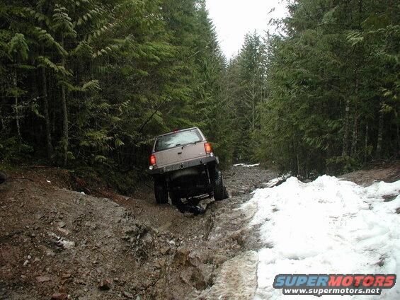 Tan SUV driving on a muddy and snowy forest trail.