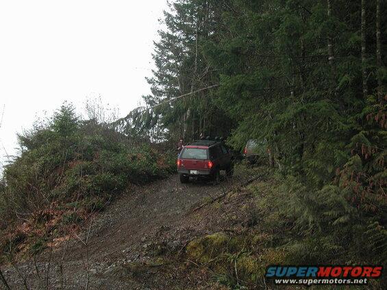 Red SUV on a steep, unpaved, wooded trail.