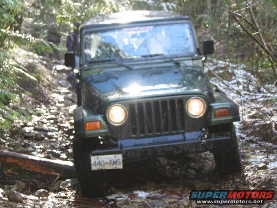 Green Jeep Wrangler driving off-road on a rocky, snowy trail.