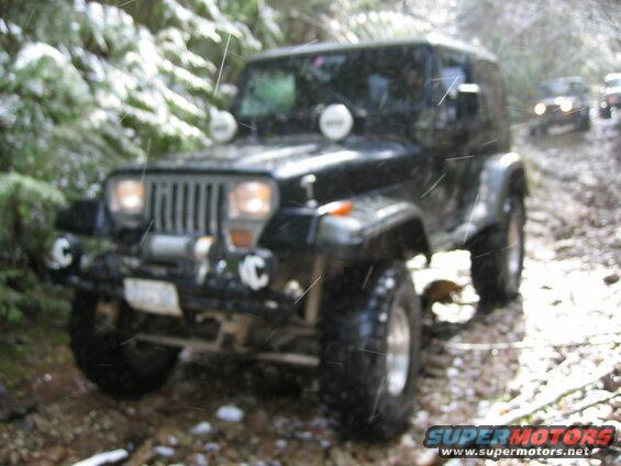 Black Jeep Wrangler driving on a muddy trail in the snow.