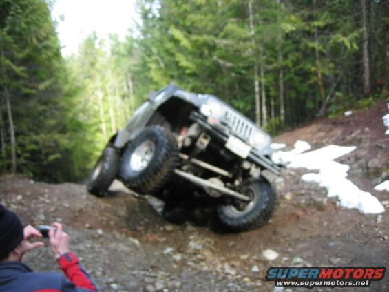 Jeep Wrangler tilted on its side on a dirt trail in a forest.