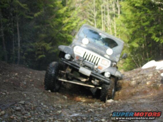 Jeep Wrangler driving up a steep, muddy, and rocky forest trail.