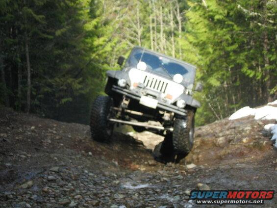 Black Jeep Wrangler off-roading on a rocky, muddy forest trail.