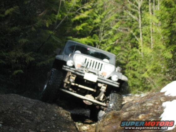 A dark Jeep Wrangler off-roading on a rocky, wooded trail.