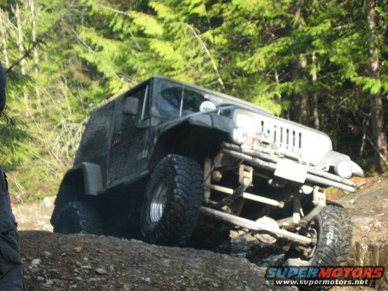 Dark Jeep Wrangler off-roading on a rocky trail with large tires.