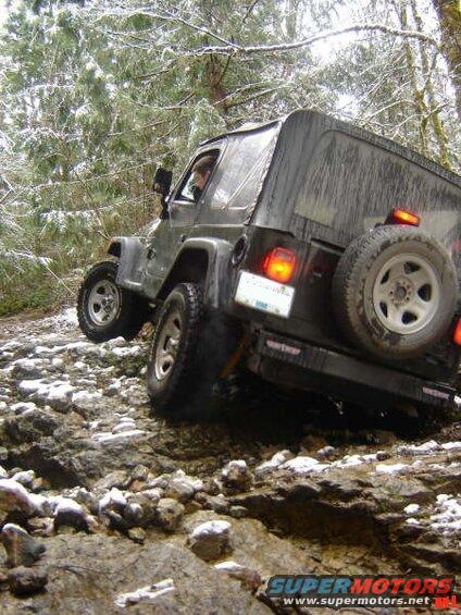 Dark Jeep Wrangler driving on a rocky trail with snow.