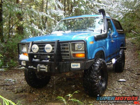 Blue 1980s Ford Bronco with snorkel and brush guard in a snowy forest.