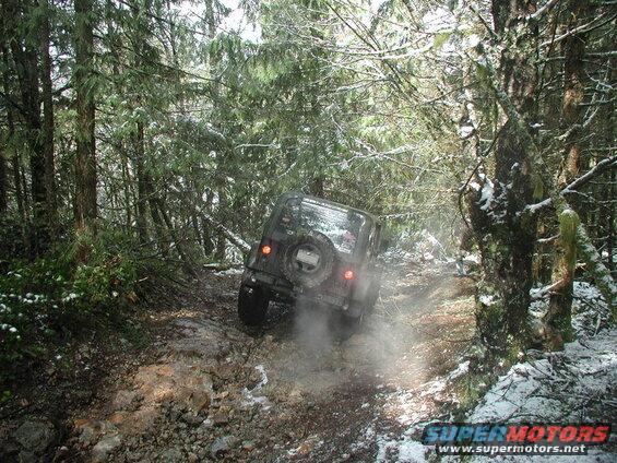 Dark Jeep Wrangler driving on a rocky, snowy forest trail.