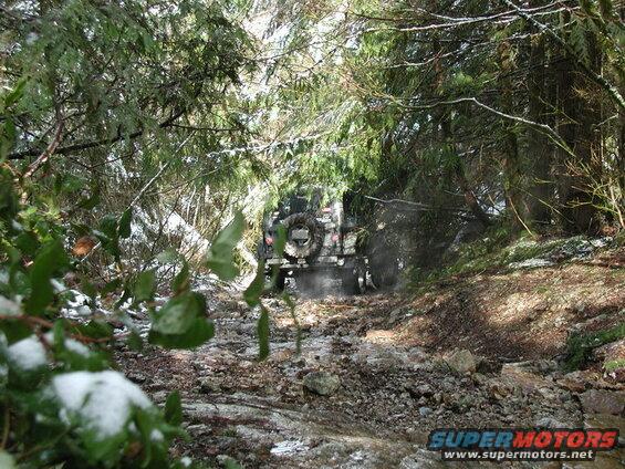 Jeep Wrangler driving on a snowy, rocky trail through a forest.