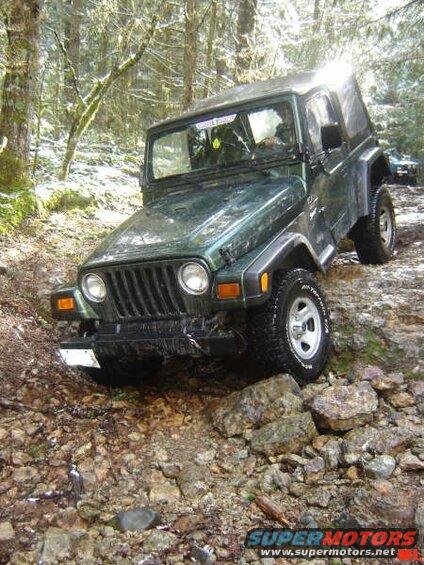 Dark green Jeep Wrangler off-roading on a rocky, wooded trail.