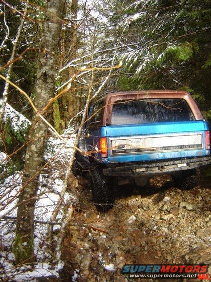 Rear view of a blue Ford Bronco on a snowy, rocky off-road trail.