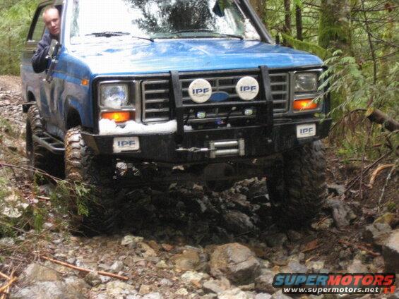 Blue Ford Bronco on a rocky trail with aftermarket bumper and lights.